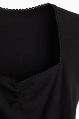 Top corto negro de punto acanalado fino de algodón. Modelo de manga japonesa con costura fruncida en el busto, escote corazón con ribete de picot y bajo recto.