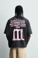 Camiseta negra de corte holgado con cuello redondo y mangas cortas. Estampado frontal y trasero con textos y figuras en color rosa.