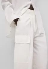 Pantalón cargo de mujer confeccionado en lino y algodón color blanco, de corte recto y tiro alto, con cierre de botón y trabillas. Presenta bolsillos laterales con solapa, bolsillos de vivo en la espalda y logo bordado en la parte trasera.