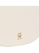 Cartera saddle mensajera color crema, con correa de textil trenzado con inscripciones de Tommy Hilfiger y la insignia brillante del monograma TH en la parte delantera.
