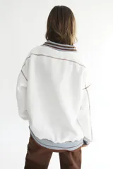 Buzo celeste con cuello polo y puños en rib color verde lima. Tiene un parche con el logo de la marca en el pecho y rayas horizontales en el ruedo.
