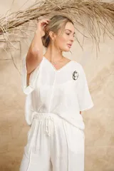 Blusa blanca de lino con escote en V, mangas cortas y detalles de punto escama en el escote y las mangas. Incluye prendedor de flor.