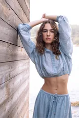 Blusa corta celeste en tejido arrugado liviano, con cuello mao, botones al frente y mangas abullonadas. Terminada con ruedo elastizado.