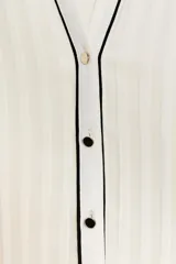Blusa blanca plisada sin mangas, con cuello redondo y cierre frontal con botones. Presenta vivos negros en cuello, sisas y botonera.
