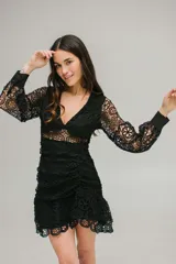 Vestido corto de encaje negro con escote en V, mangas largas abullonadas y falda con volados. Presenta cierre invisible en la espalda.
