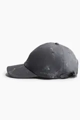 Gorra gris con estampado jaspeado, logo plateado en el frente, ojales bordados y cordón elástico ajustable en la parte trasera.