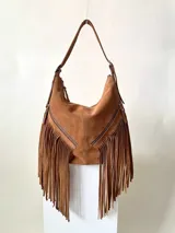 Bolso bandolera marrón de cuero gamuzado con flecos largos, cierre superior con cremallera y dos bolsillos frontales con cierre.