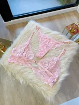 Conjunto de lencería rosa de encaje floral, compuesto por un corpiño triangular con breteles regulables y cierre frontal, y una tanga regulable.