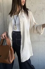 Camisa beige con bordados florales blancos, de corte recto y mangas largas con puños enrollados.
