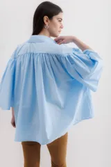 Camisa celeste de algodón con corte amplio, cuello camisero y mangas largas con puños abullonados.
