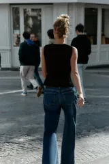 Top negro de punto, sin mangas, con cuello redondo. Presenta costuras marcadas en el frente y un bajo con abertura frontal que simula un peplum ajustado.