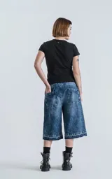 Bermuda larga de denim azul con lavado ácido y efecto desgastado. Presenta un calce oversize, talle alto con cinturón de tela a juego y ruedos deshilachados.