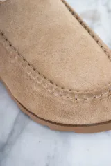 Zueco color beige de gamuza, con plantilla de corcho, detalle de costuras en la parte delantera y tira trasera ajustable con hebilla.