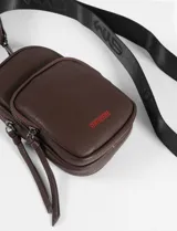 Porta celular negro de cuero sintético con bolsillo frontal y correa larga ajustable.