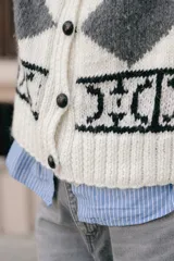 Chaleco de lana tejido a mano con diseño jacquard en negro, blanco y gris. Tiene cuello redondo y cierre frontal con botones de cuero.