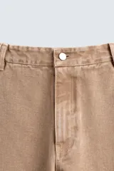 Pantalón de jean color beige, de corte ancho y tiro medio, con cinco bolsillos, efecto lavado y cierre frontal con cremallera y botón.