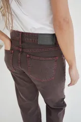 Pantalón de jean marrón de corte recto y tiro medio, con costuras en color naranja y texto estampado en el bolsillo trasero.