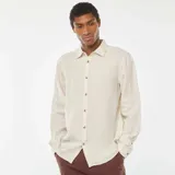 Camisa de lino color beige claro, de corte regular, con cuello clásico y mangas largas con puños abotonados.