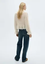 Blusa color crema con estampado de lunares, escote en V con volantes y lazos, mangas largas abullonadas con puños elásticos y corte peplum.