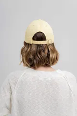 Gorra de béisbol color amarillo pastel, con visera curva y logo de Peach bordado en el frente. Ajustable en la parte trasera.