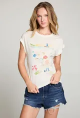 Remera color crema con estampado de playa con sombrillas, reposeras y un velero.