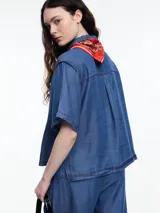 Camisa negra de manga corta confeccionada en denim liviano de tencel, de calce cuadrado y relajado. Presenta cierre frontal con tapeta escondida y costuras en color contraste.