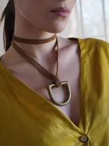 Collar con tira de cuero color suela y dije metálico dorado en forma de estribo.