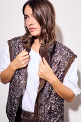 Chaleco reversible de algodón con acabado lavado y diseño acolchado con pespuntes ondulados. Presenta cuello alto con cordón ajustable, cierre frontal de cremallera y botones a presión, bolsillos delanteros tipo parche y cordón de ajuste en el bajo.