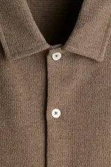 Camisa marrón de punto con textura, corte regular, cuello inglés, tapeta lisa, canesú en la espalda, bajo recto con aberturas laterales y manga corta.