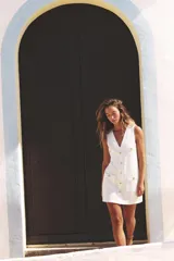 Vestido corto blanco de sarga, con escote en V, sin mangas, bolsillos frontales con botón dorado y cierre frontal con botones metálicos dorados en relieve.