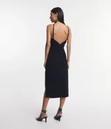 Vestido midi negro de bengalina, sin mangas, con breteles finos, escote halter, pliegues, abertura lateral y cierre por cremallera en la espalda.