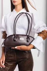 Cartera baguette negra con textura símil cuero de reptil, doble asa corta y logo metálico plateado de la marca Agnes.