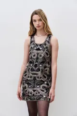 Vestido corto negro con cuello redondo y sin mangas, completamente bordado con mostacillas, piedras y lentejuelas. Tiene corte recto y calados que acompañan el diseño.