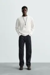 Camiseta blanca de manga larga con cuello redondo y textura cuadriculada.