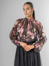 Camisa de seda italiana con estampado floral en tonos rosados, marrones y verdes. Presenta cuello alto con volados que caen en cascada sobre el frente y mangas largas abullonadas con puños ajustados.