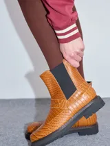 Bota Chelsea de cuero negro con estampado de cocodrilo, elástico lateral y suela de goma con pespuntes azules.