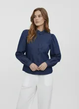 Camisa de denim color azul oscuro, de manga larga con hombros abullonados y puños ajustados con botón. Presenta cuello clásico y cierre frontal de botones.