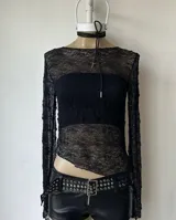 Top de encaje negro con mangas largas y corte irregular en el ruedo.