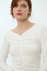 Remera de tela rib color blanco, con manga larga, escote en forma de V y frunce frontal.