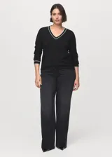 Jersey de punto fino color negro con cuello de pico y ribetes en contraste blanco en el cuello y puños. Diseño recto y manga larga.