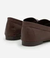 Mocasín de cuero color marrón con puntera fina, detalle de pliegues y tachuelas plateadas.