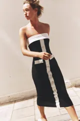 Vestido midi negro de tejido elástico, con escote recto y hombros descubiertos. Presenta falsos bolsillos con botón en el delantero, acabados a contraste en blanco y cierre frontal con botones.