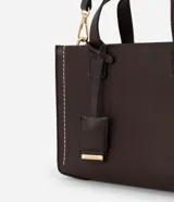 Cartera tipo satchel estructurada de color marrón oscuro, con costuras decorativas en contraste color crema en los laterales. Posee asas superiores cortas y una correa larga ajustable y desmontable. Los herrajes son de color dorado.
