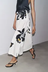 Falda midi de tiro alto confeccionada en hilatura de algodón color blanco con estampado floral en negro y amarillo. Tiene cierre con cremallera oculta en la costura y detalle de botones en la cintura.
