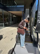 Bolso tote marrón de gabardina con detalles de cuero negro, asas cortas y cierre superior.