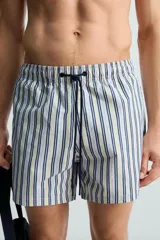 Bañador de hombre confeccionado en tejido técnico con textura. Diseño a rayas verticales en tonos azul y blanco. Cintura elástica ajustable con cordón. Bolsillos laterales y detalle de bolsillo trasero de solapa. Bajo con aberturas laterales. Forro interior.