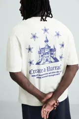 Camiseta blanca de corte holgado con cuello redondo y mangas cortas. Estampa en el pecho con la frase "Create a Narrative" en azul.