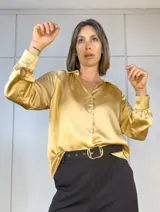 Camisa color dorado de satén plisado, con cuello clásico, cierre frontal con botones y mangas largas con puños abotonados.