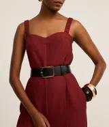 Mono de mujer color rojo oscuro (bordó), de corte recto y pierna ancha, con escote corazón y tirantes anchos con elástico. Presenta pliegues frontales que caen rectos hasta el ruedo.