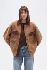 Campera estilo camisa (shacket) de tejido tipo borrego o sherpa color crema, con cuello y tapeta de pana marrón. Posee dos bolsillos frontales con tapa y botones a presión.